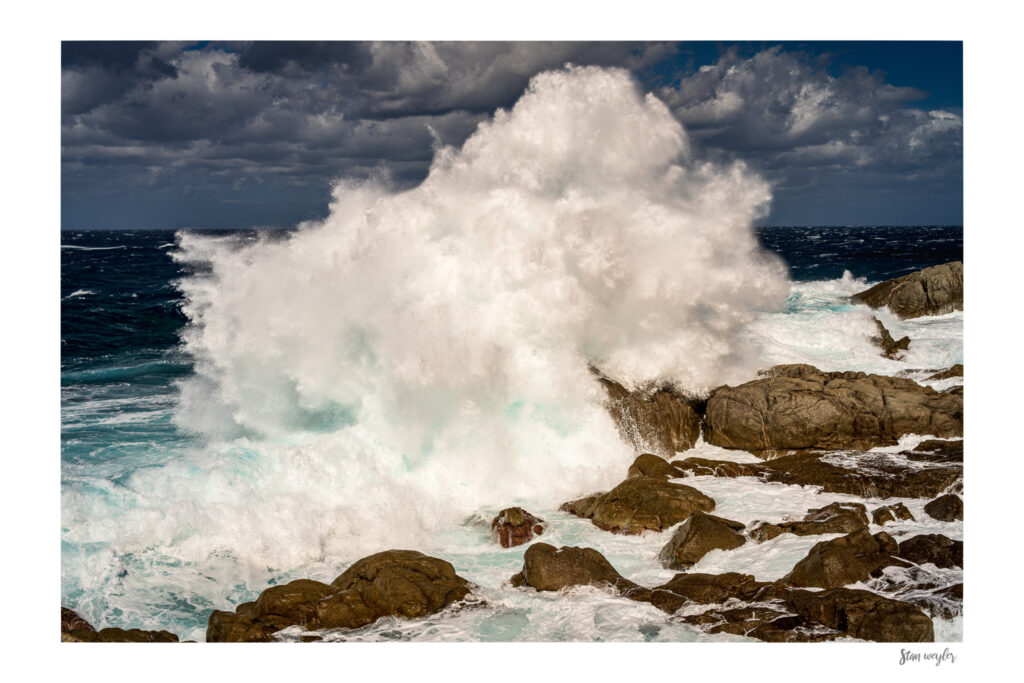 Dramatic Corsica Coastal Wave Print, Stormy Sea Splash, Fine Art Beach Photo (Archival Print) Fine art coastal photograph of a massive ocean wave crashing against rocky shores in northern Corsica by Stan Weyler. High-speed detail capture showing a huge white sea spray explosion and turquoise ocean water under a dramatic stormy sky. Seascape wall art for modern living rooms, beach houses, and offices, printed on museum-quality matte paper.