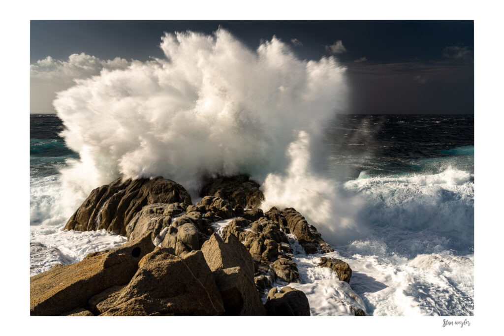 Dramatic Corsica Seascape Print, Golden Hour Crashing Wave Wall Art Fine art seascape photograph of a storm wave crashing on the rocky coast of Corsica at sunset by Stan Weyler. Golden hour light illuminating fine strands of sea spray bursting into the air against a dark ocean sky. Coastal wall decor for modern living rooms, offices, and gallery displays, printed on museum-quality archival matte paper.
