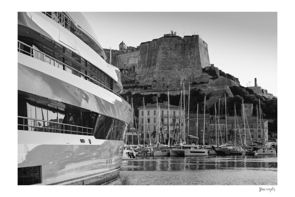 Bonifacio Corsica Black and White Print – Historic Citadel, Superyacht Photography, Maritime Wall Art by Stan Weyler Art Fine art black and white artistic photograph of the Bonifacio harbor with the famous Citadel fort in the background. The monochrome print captures the powerful contrast between the ancient medieval citadel perched high on the cliffs and the sleek, modern lines of a massive superyacht in the foreground. The high-contrast maritime composition beautifully highlights Corsica's history and contemporary luxury by Stan Weyler Art